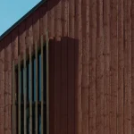 Närbild av en fasad med stående träpanel mot blå himmel