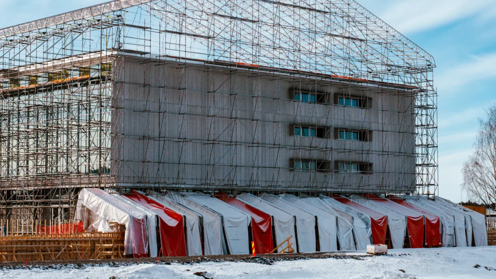 Flerbostadshus inklätt i byggnadsställningar och väderskydd vintertid