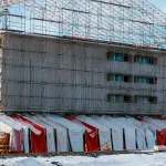 Flerbostadshus inklätt i byggnadsställningar och väderskydd vintertid