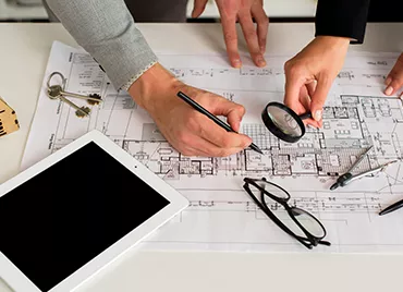 Två personer som granskar en planritning med penna och förstoringsglas